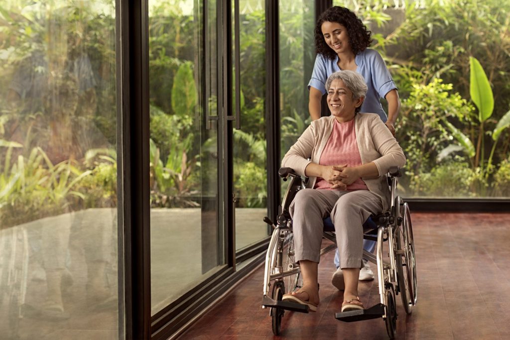 A young woman helping an Indian senior in a wheelchair during a stage of dementia.