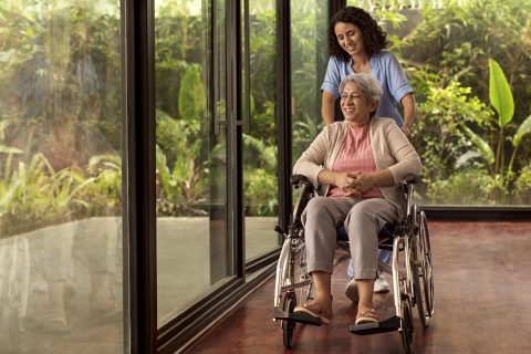 A young woman helping an Indian senior in a wheelchair during a stage of dementia.