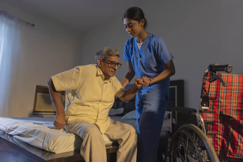 A nurse helping an elderly man sit in his wheelchair, showing the impact of dementia on older adults in India.