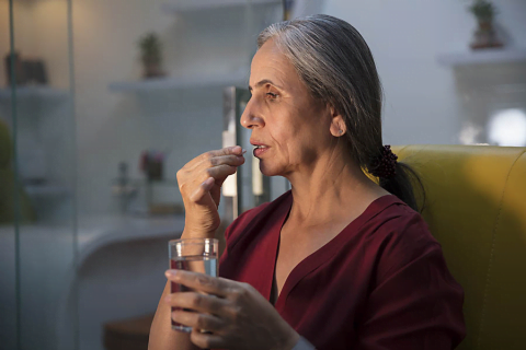 An elderly woman consuming a multivitamin for brain health with a glass of water.